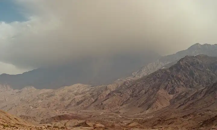 La cordillera de 25 km se dividió, ondas sísmicas radiando de epicentro, terreno rocoso agrietado y destrozado, nubes de polvo que suben al aire, temblores que afectan las remotas montañas, paisaje de Atlas Mountains en desarray