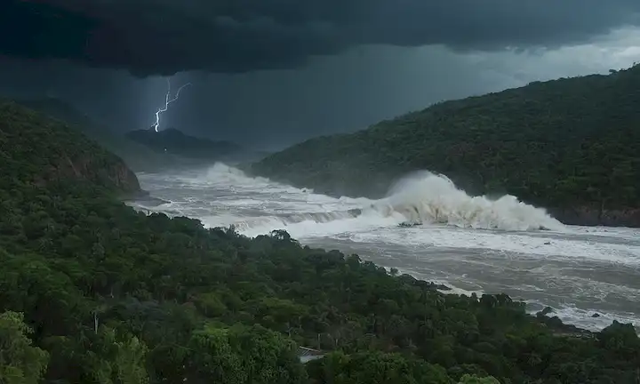 animación 3D de una ola masiva de tsunamis que choca contra un paisaje mexicano, con un lecho de ríos en primer plano, bosques densos y colinas en el fondo, agua que brota sobre edificios e infraestructura, caos y destrucción en las secuelas, cielos oscuros con relámpagos, ruidos lejanos de truenos