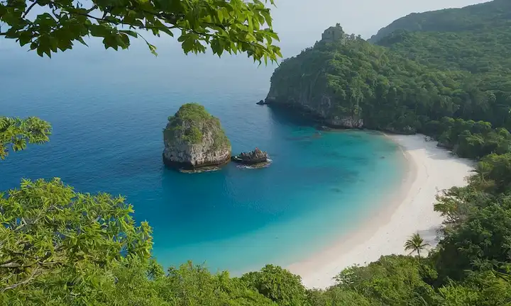 una isla serena, azul, playa en forma de crescente, exuberante vegetación, unas cuantas rocas dispersas, un naufragio en el fondo, suave ambiente de la miseria, cálida luz del sol, débil esbozo de un ojo símbolo en una superficie rocosa, sutil sentido del misterio, tranquilo y tranquilo paisaje