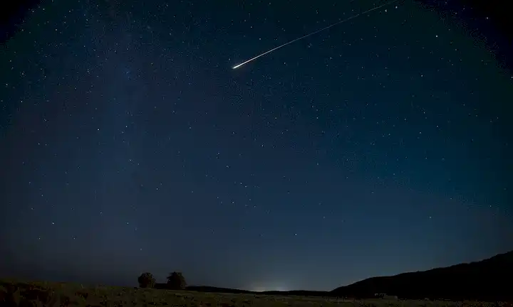 Un cielo nocturno sereno con estrellas brillantes, unas pocas nubes agitadas, una débil estrecha de luz que representa la órbita de las estaciones espaciales internacionales, un pequeño grupo
<center><img decoding=