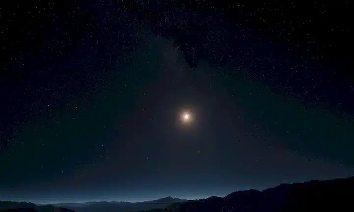 Una vasta escena del espacio oscuro con un pequeño punto, distante Tierra, contorno del sistema solar, estrellas que brillan, y un resplandor sutil del Sol